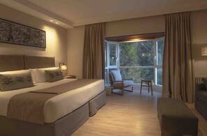 Quarto com cama grande, uma cadeira, um sofá e vista para o exterior.