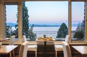 A dining area with a table set for two, overlooking a lake with mountains in the distance. - La Cascada Casa Patagónica by DON (San Carlos de Bariloche)