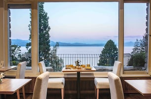 Uma área de refeições com uma mesa posta para dois, com vista para um lago e montanhas ao fundo.