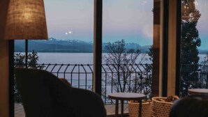 A room with a view of a lake and mountains, featuring a chair, small round tables, and a lamp. - La Cascada Casa Patagónica by DON (San Carlos de Bariloche)