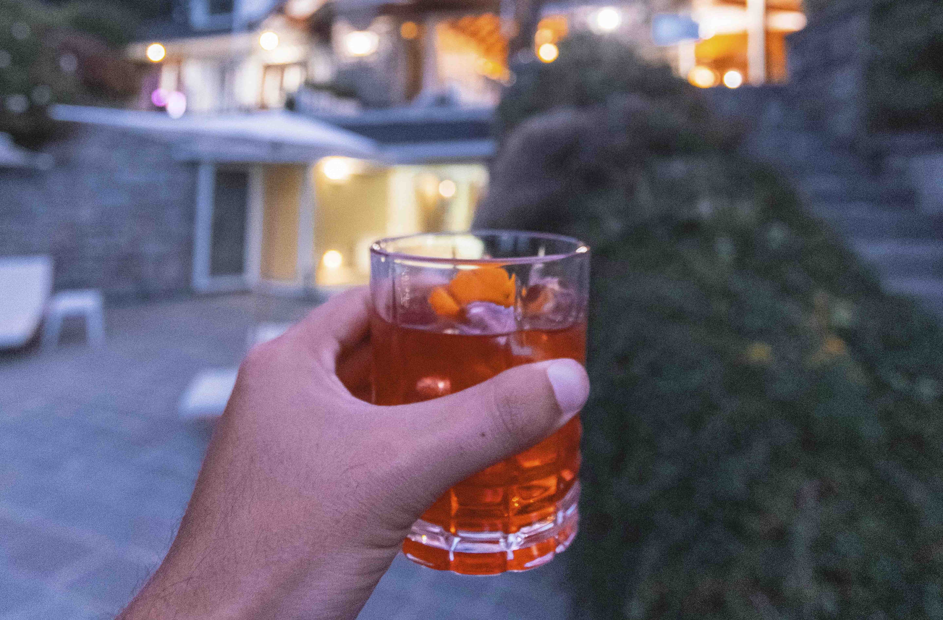 A hand holding a glass with a beverage and an orange slice.