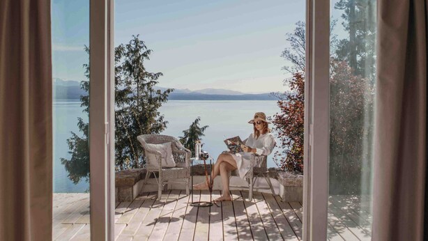 A room with a large window overlooking a lake, furnished with wicker chairs and a small table. - La Cascada Casa Patagónica by DON (San Carlos de Bariloche)