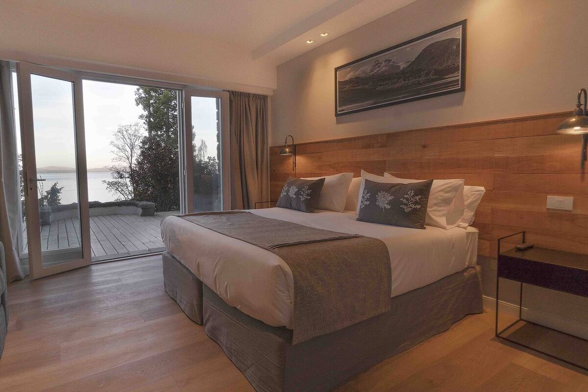Ein Schlafzimmer mit einem großen Bett, einem Holzkopfteil, einem Nachttisch und Blick ins Freie.