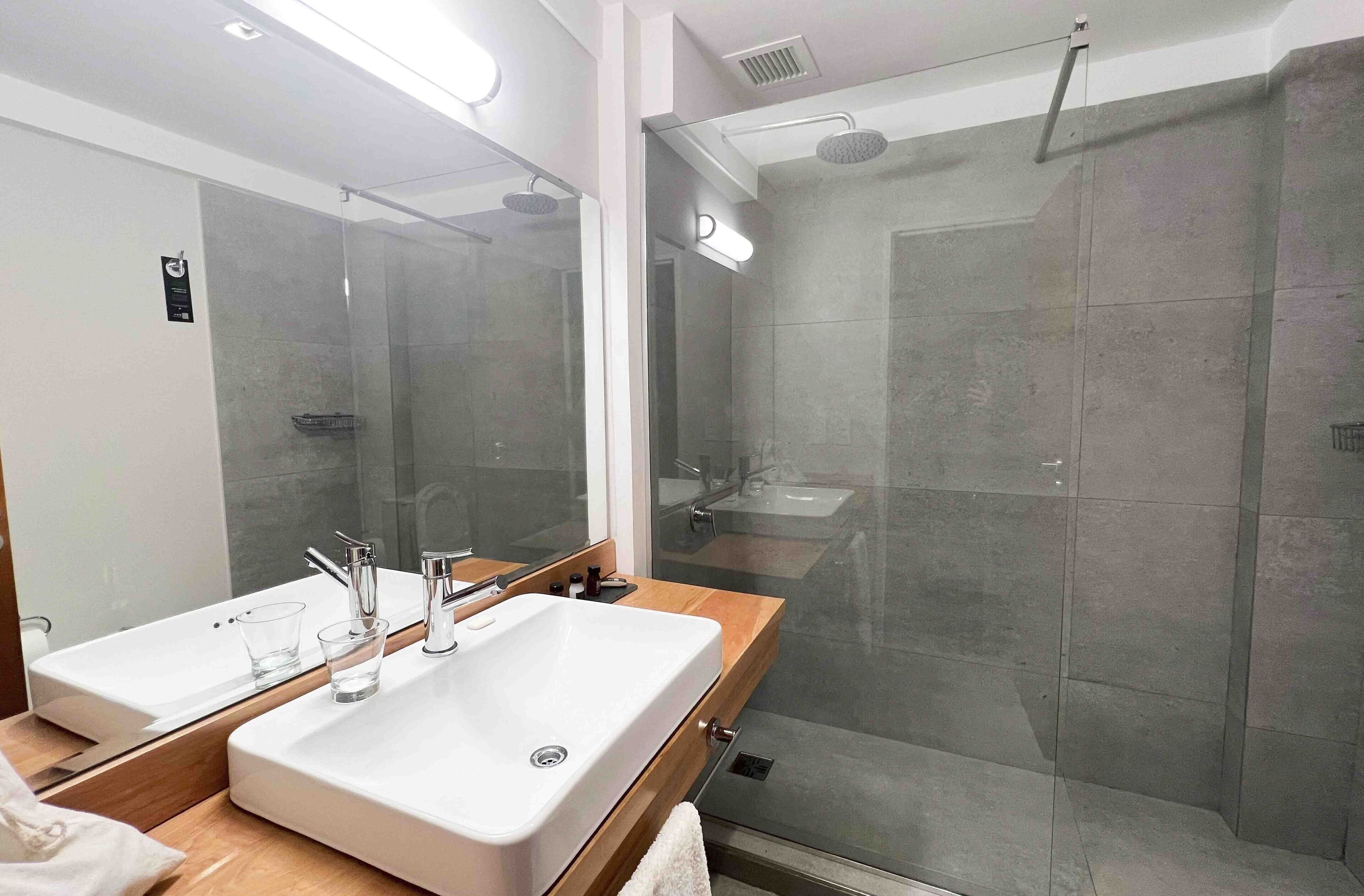 A modern bathroom with a large mirror, two sinks, and a glass-enclosed shower.