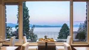 A dining area with a table set for two, overlooking a lake with mountains in the distance. - La Cascada Casa Patagónica by DON (San Carlos de Bariloche)