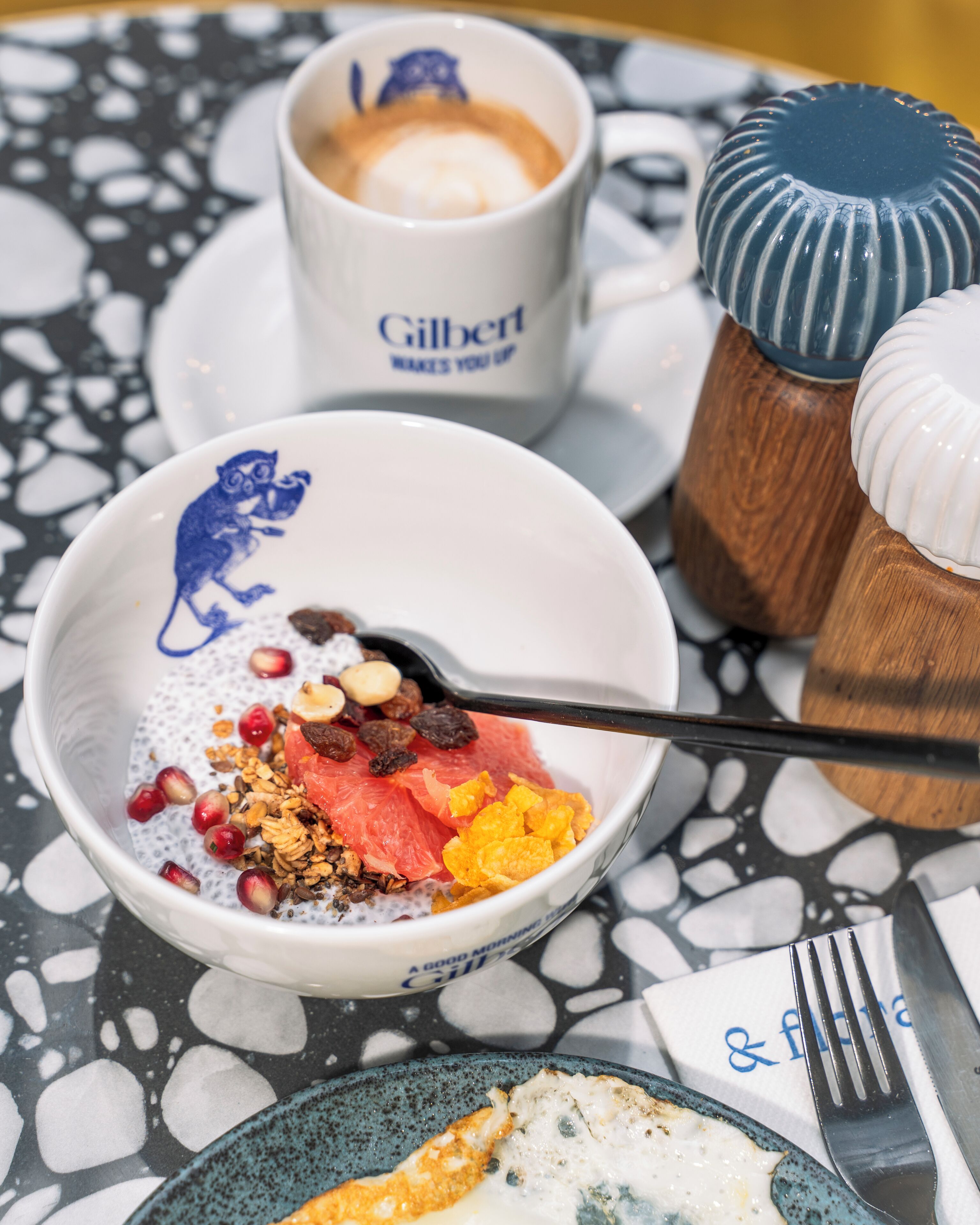 A breakfast setting with a bowl of cereal, a cup of coffee, and a plate with a fried egg.