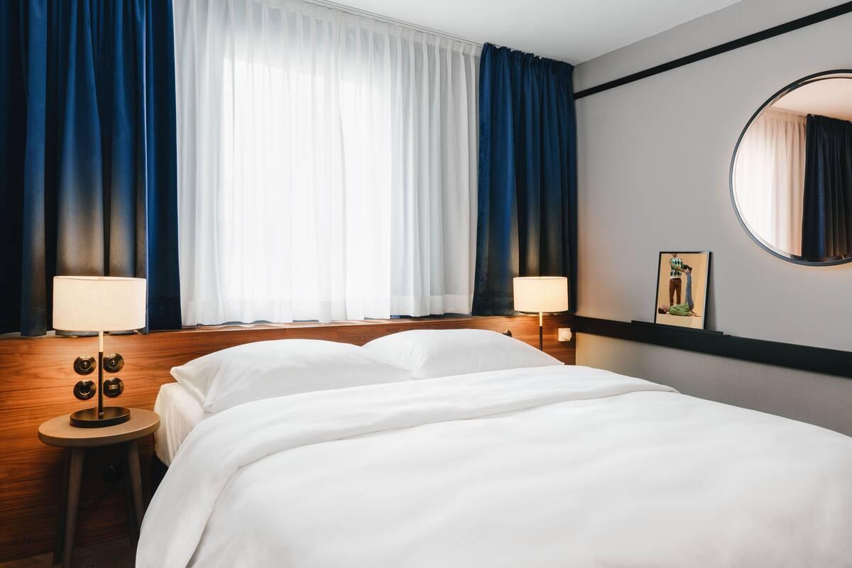 Een hotelkamer met een groot bed, twee bedlampen, een ronde spiegel en een schilderij aan de muur.