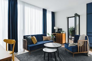 Uma sala de estar moderna com um sofá azul, uma cadeira de madeira, uma pequena mesa redonda e um móvel com uma televisão.
