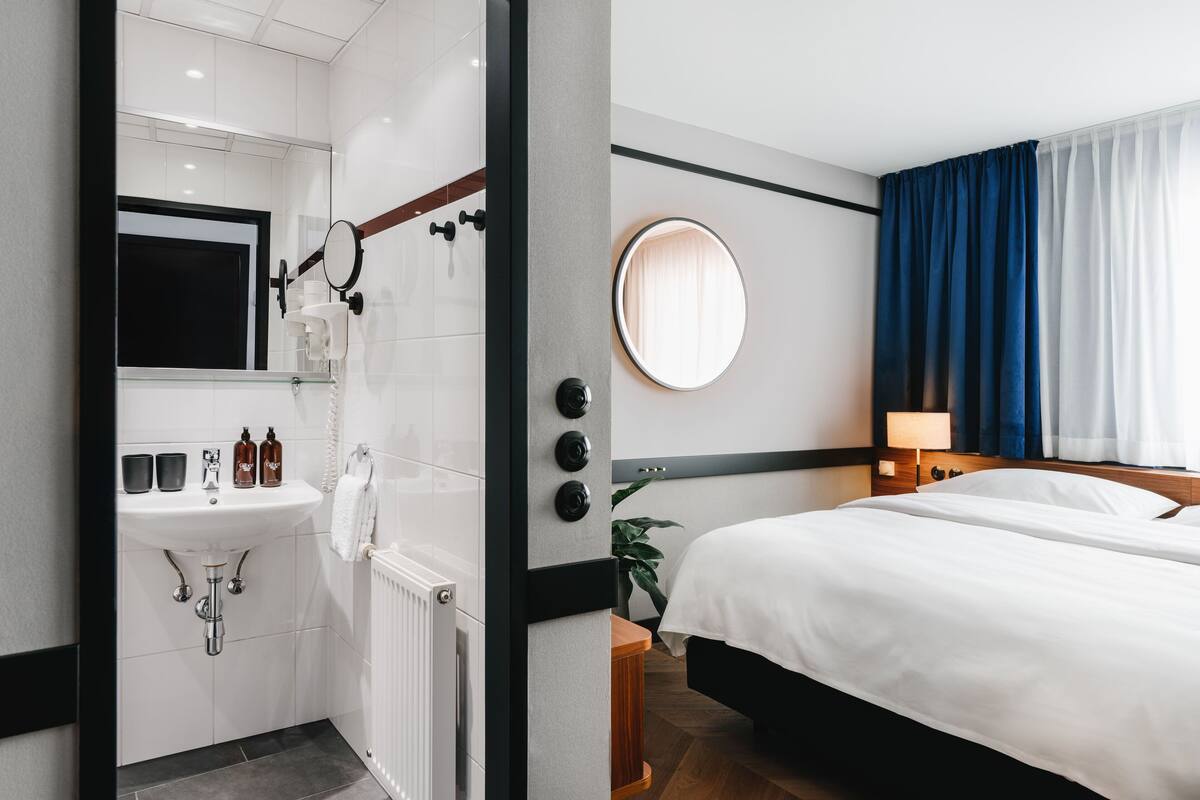 Een hotelkamer met een bed, een ronde spiegel, een wastafel en een raam met gordijnen.