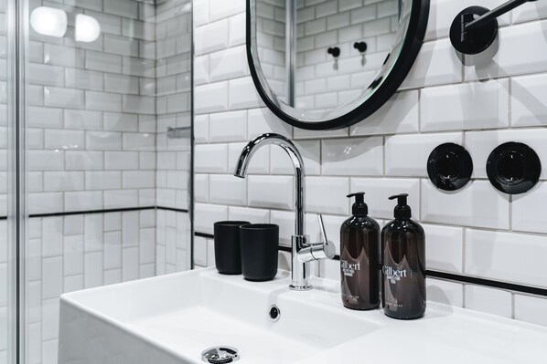 A modern bathroom with a white sink, black soap dispensers, and a large mirror.