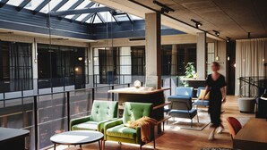 A spacious indoor area with a high ceiling, large windows, and a mix of seating arrangements including green and orange chairs. - Hotel Gilbert (Vienna)