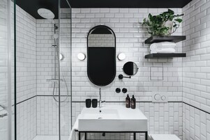 Casa de banho moderna com azulejos brancos, uma sanita branca, um espelho preto e uma planta numa prateleira.