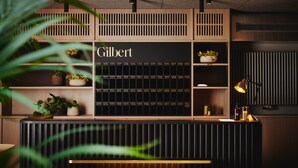 A modern reception desk with a blackboard displaying room numbers, surrounded by wooden shelving with potted plants. - Hotel Gilbert (Vienna)