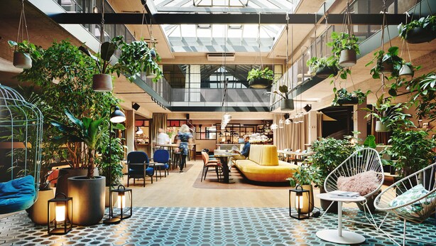 A spacious indoor area with hanging plants, seating, and a patterned floor. - Hotel Gilbert (Vienna)