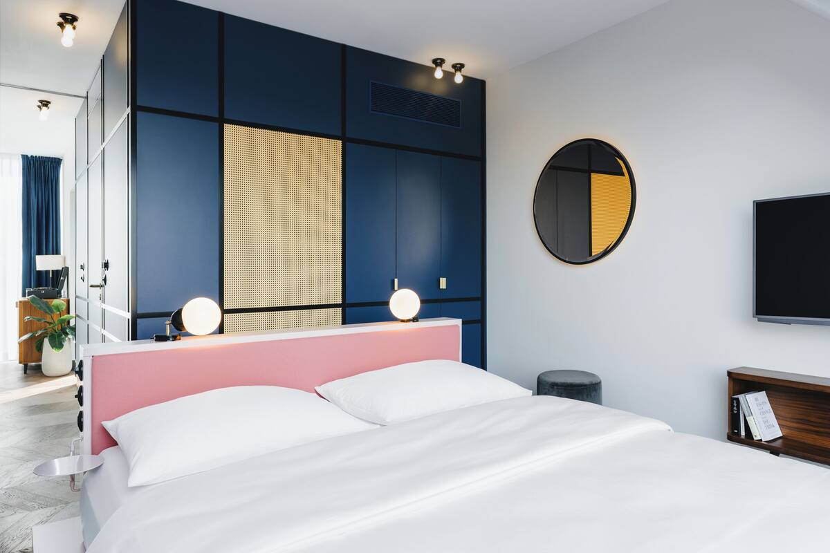 Een moderne slaapkamer met een groot bed, een nachtkastje met spiegel en een aan de muur bevestigde televisie.