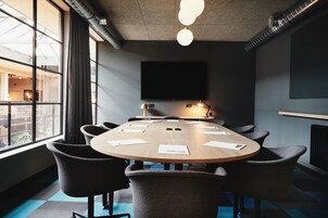 Uma sala de conferência com uma mesa redonda, cadeiras, uma televisão de tela plana e uma janela com cortinas.