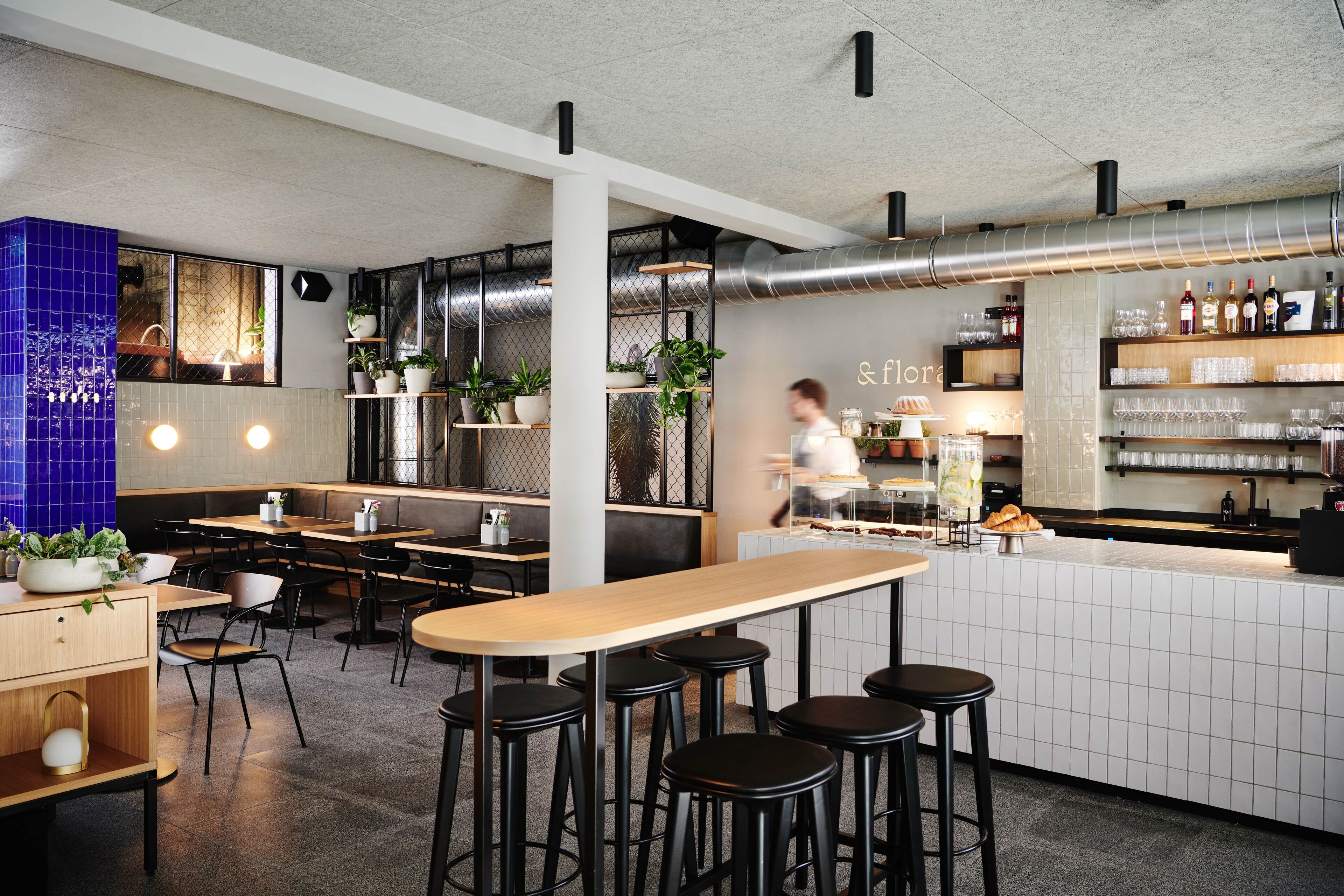 Un interior de restaurante moderno con una zona de bar, asientos y un mostrador que exhibe comida y bebidas.