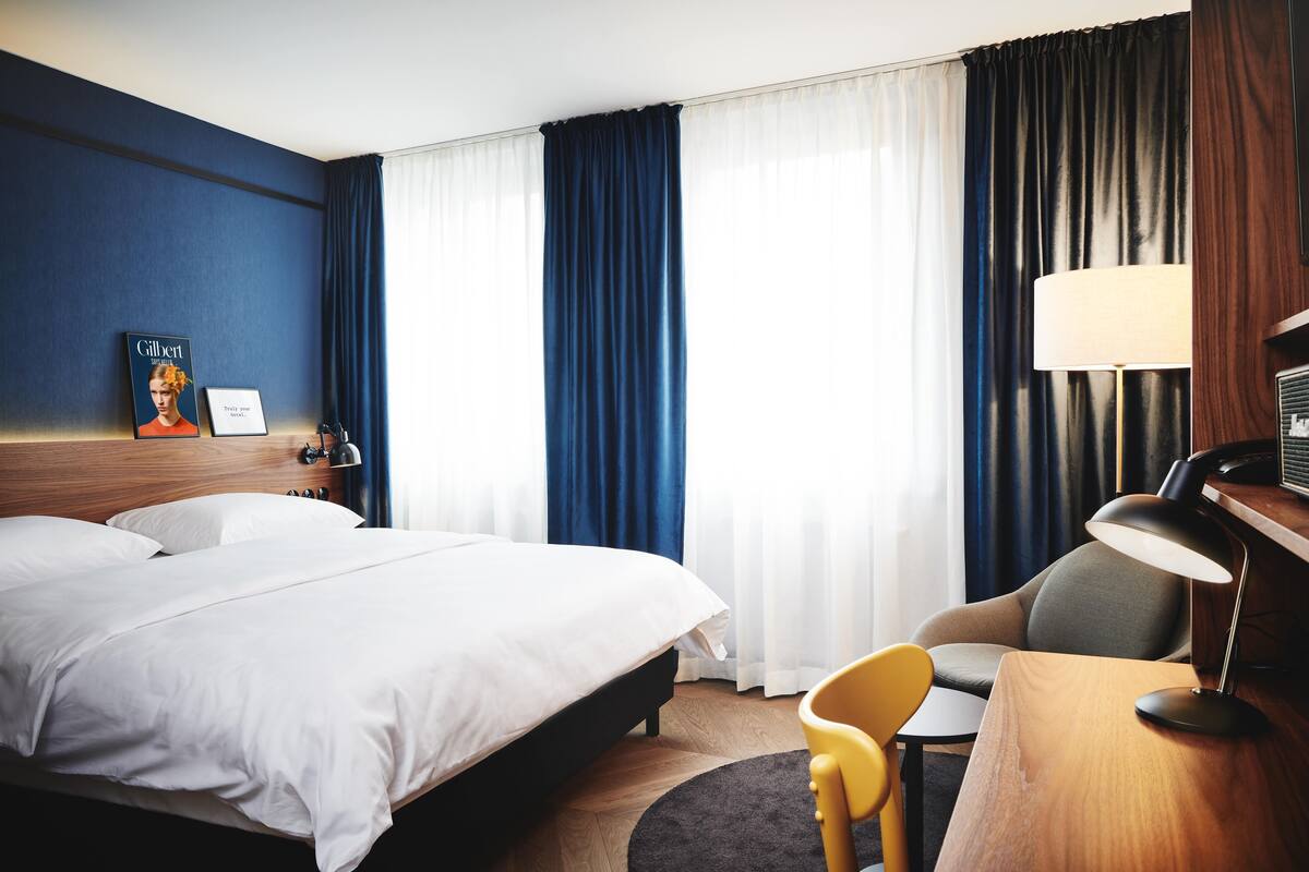 Een hotelkamer met een groot bed, een bureau met een lamp, een stoel en een fotolijst aan de muur.