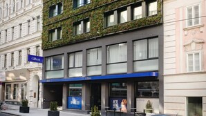 A modern building with a green facade, multiple windows, and a blue storefront. - Hotel Gilbert (Vienna)