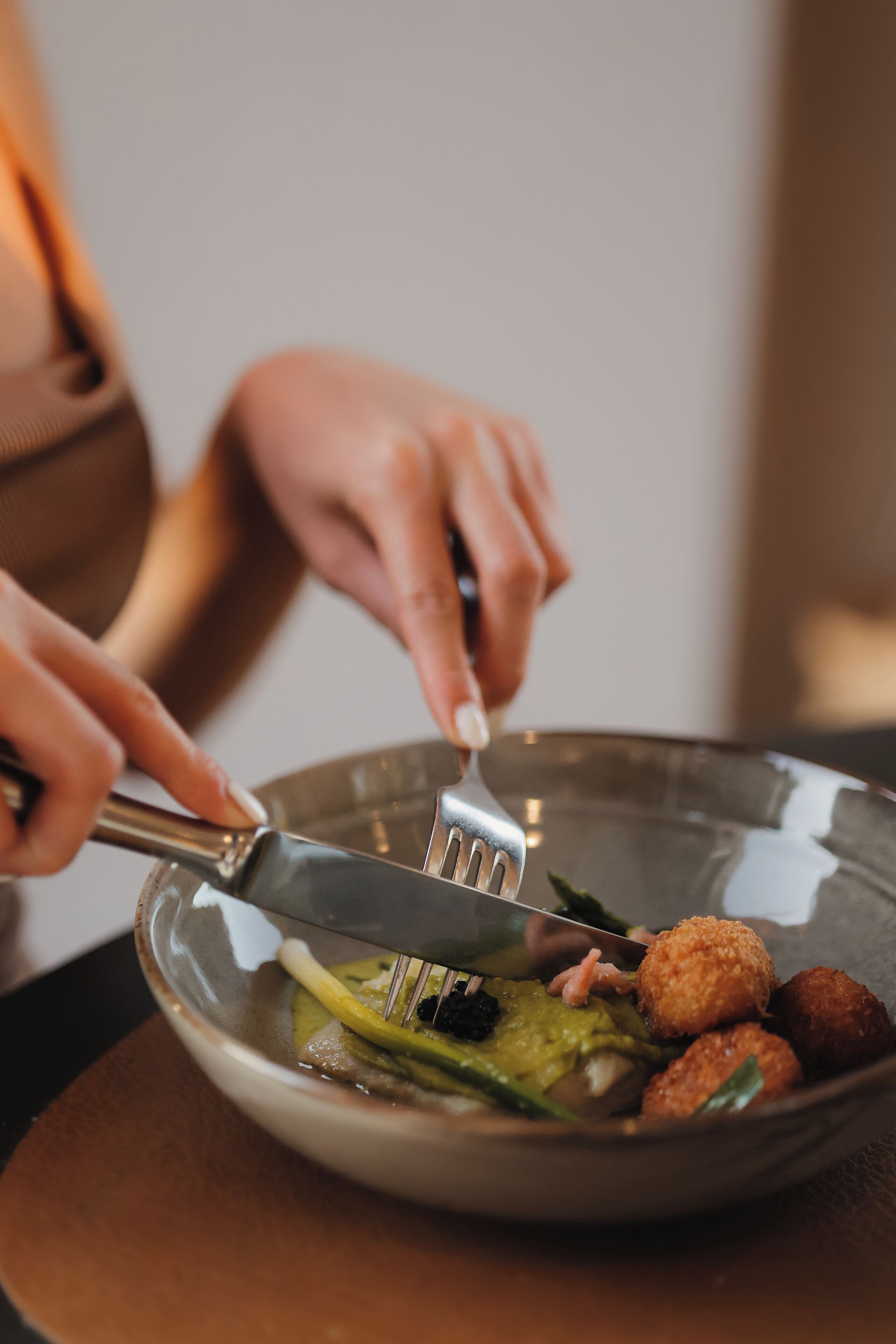 Una persona usando un tenedor y un cuchillo para comer de un plato con diferentes alimentos.