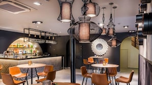A modern bar area with round tables and chairs, a bar counter with a variety of bottles, and unique hanging light fixtures. - Martin's Château du Lac (Rixensart)