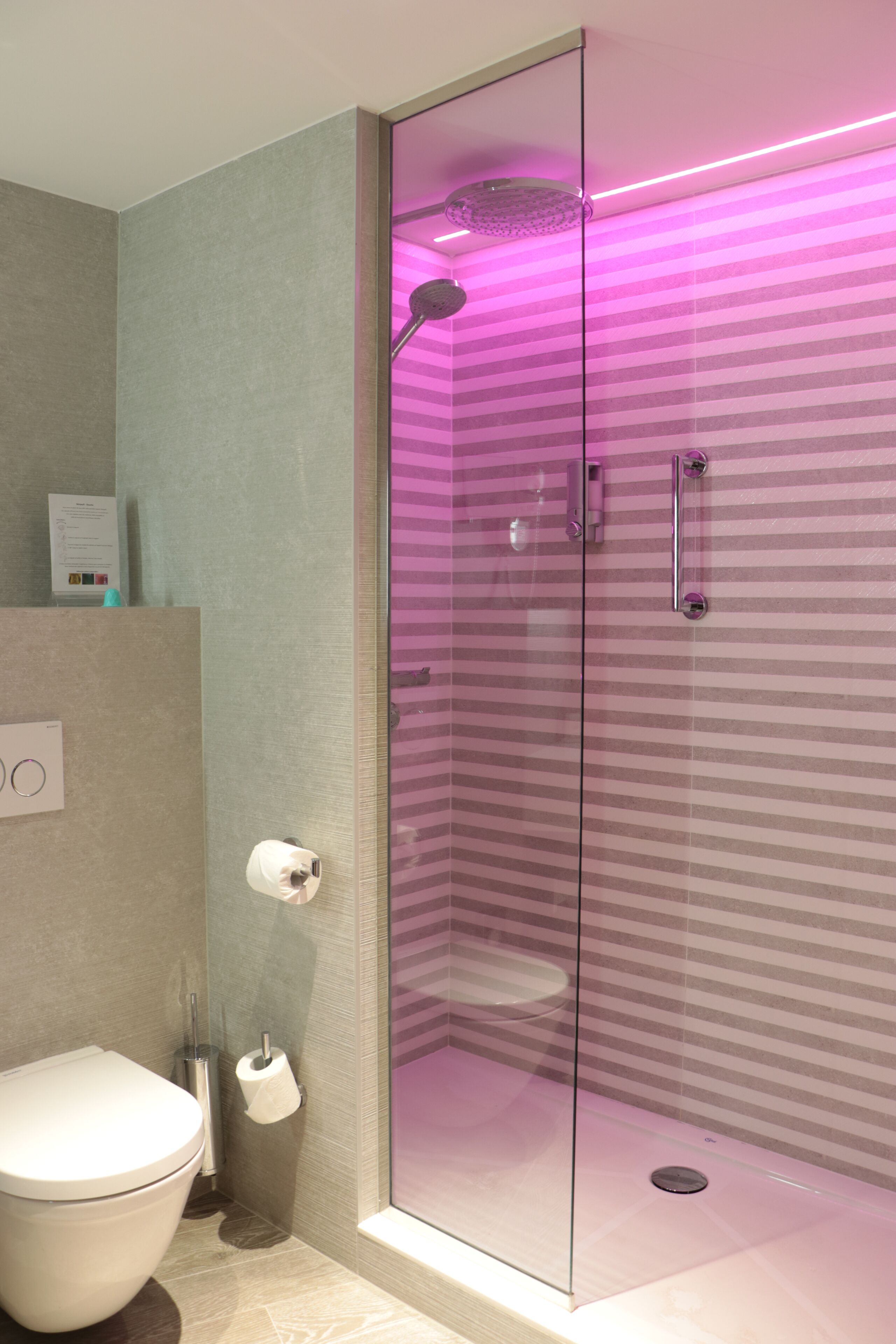 Une salle de bain moderne dotée d’une douche à parois de verre, de toilettes et d’un sèche-mains.