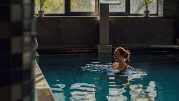 Una persona nadando en una piscina con ventanas amplias y plantas en macetas.