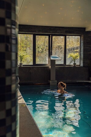 Una persona nadando en una piscina con ventanas amplias y plantas en macetas.