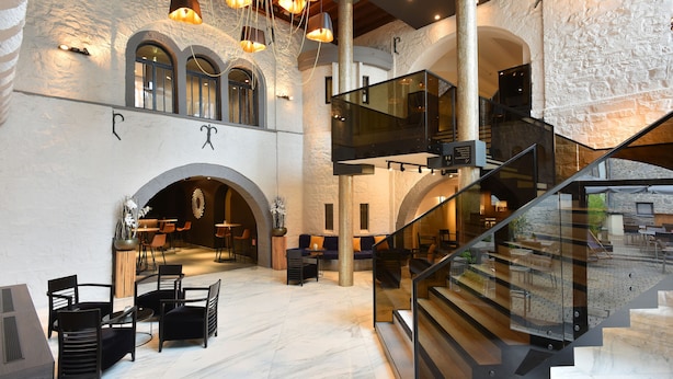 A spacious lobby with a high ceiling, stone walls, and a modern staircase.