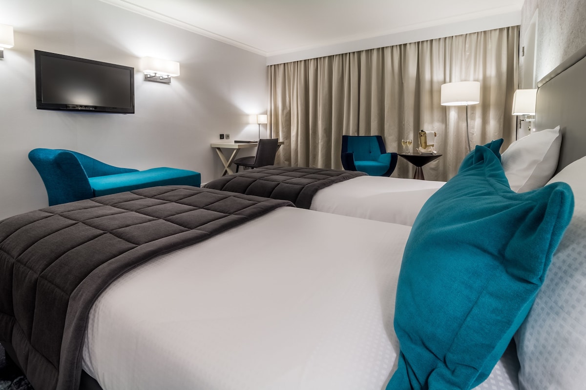A hotel room with two beds, a TV, a desk, and a chair.
