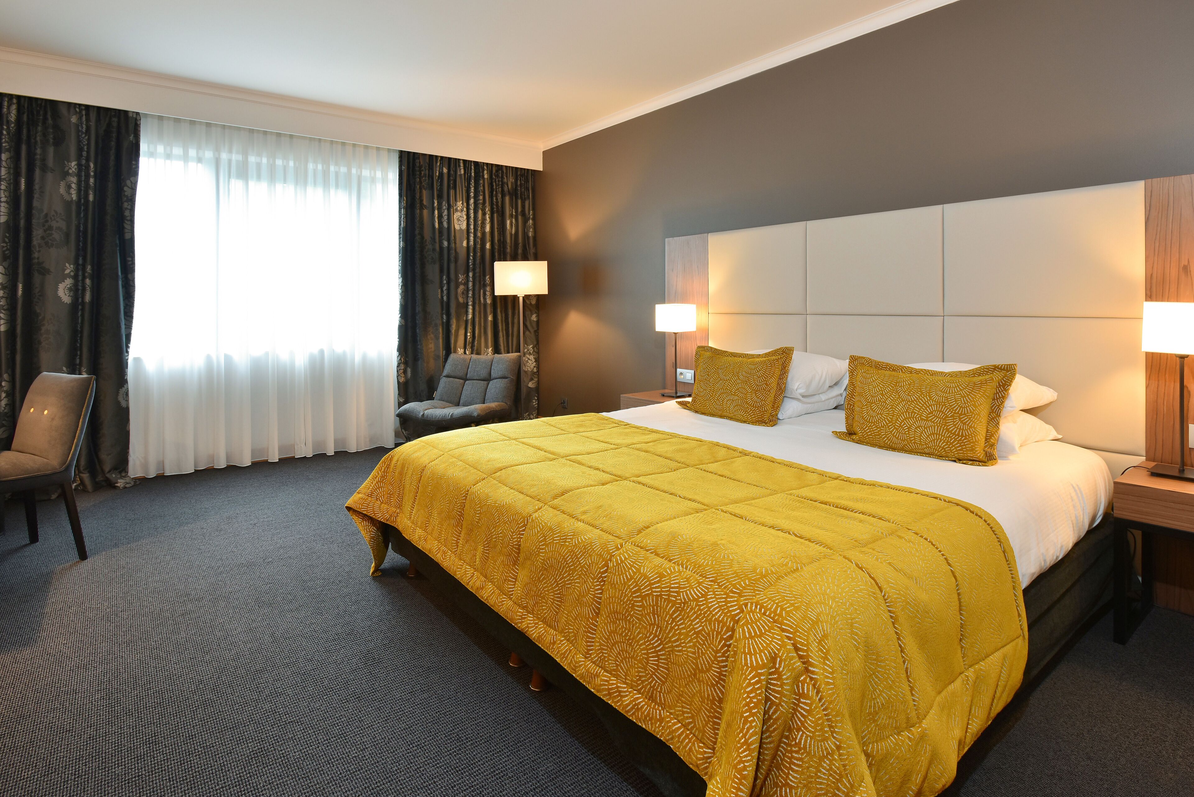 A hotel room with a large bed, two bedside lamps, a chair, and a window with curtains.