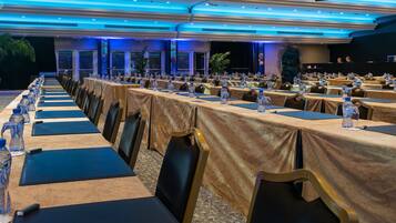 Un salón de conferencias con largas mesas, sillas y botellas de agua.