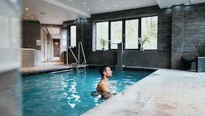 A man in a swimming pool with a view of the outdoors through large windows.