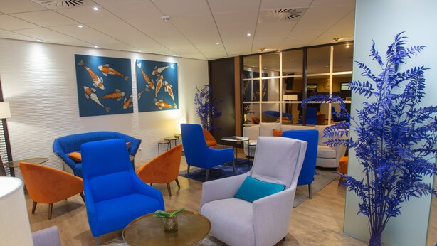 Un vestíbulo moderno con sillones azul y blanco, una mesa redonda con una planta, y arte con peces koi en la pared.