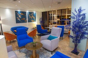 A modern lobby with blue and white armchairs, a round table with a plant, and artwork of koi fish on the wall.