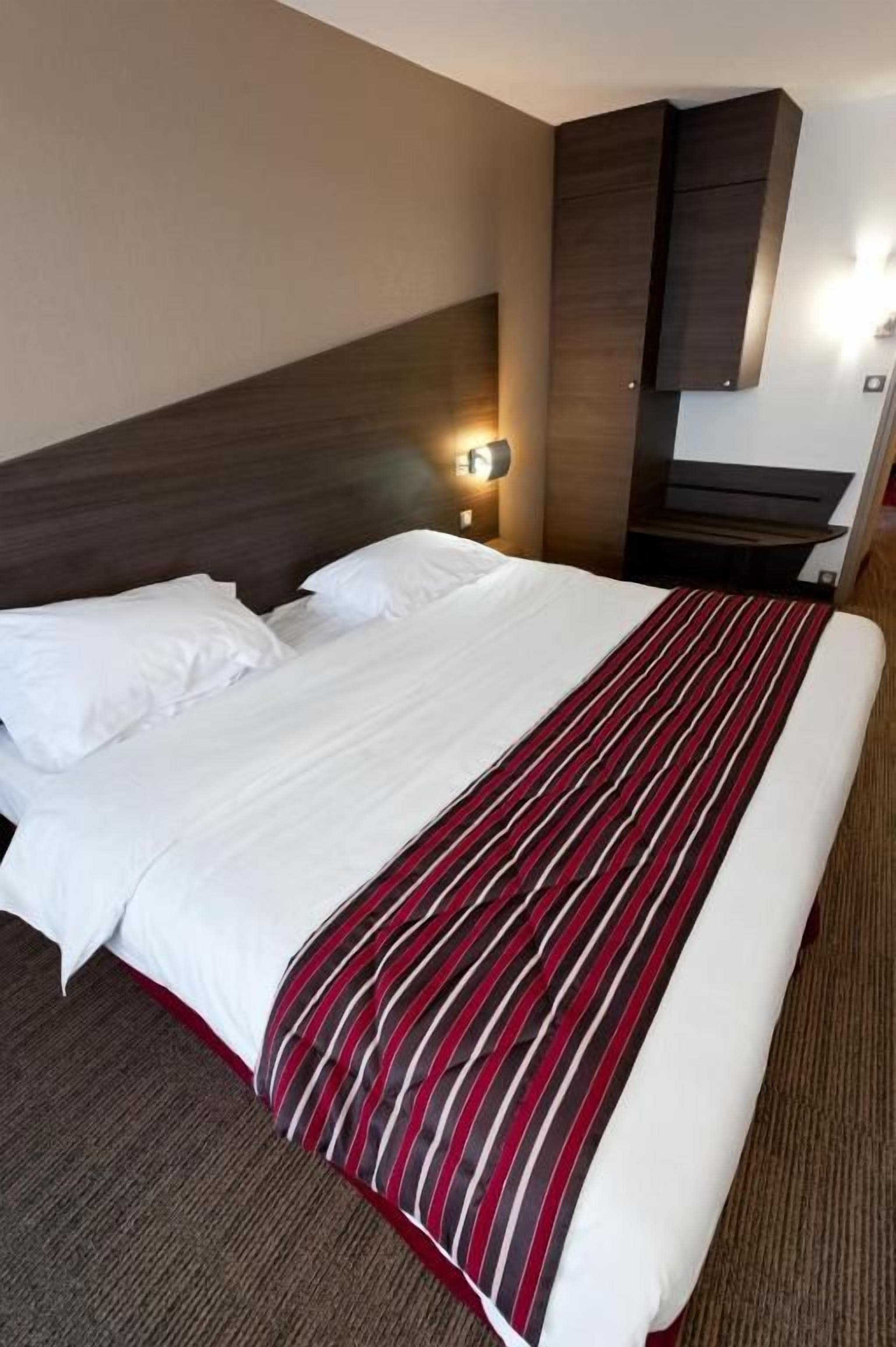 Habitación de hotel con una cama grande, cabecera, televisor montado en la pared y mesita de noche con lámpara.