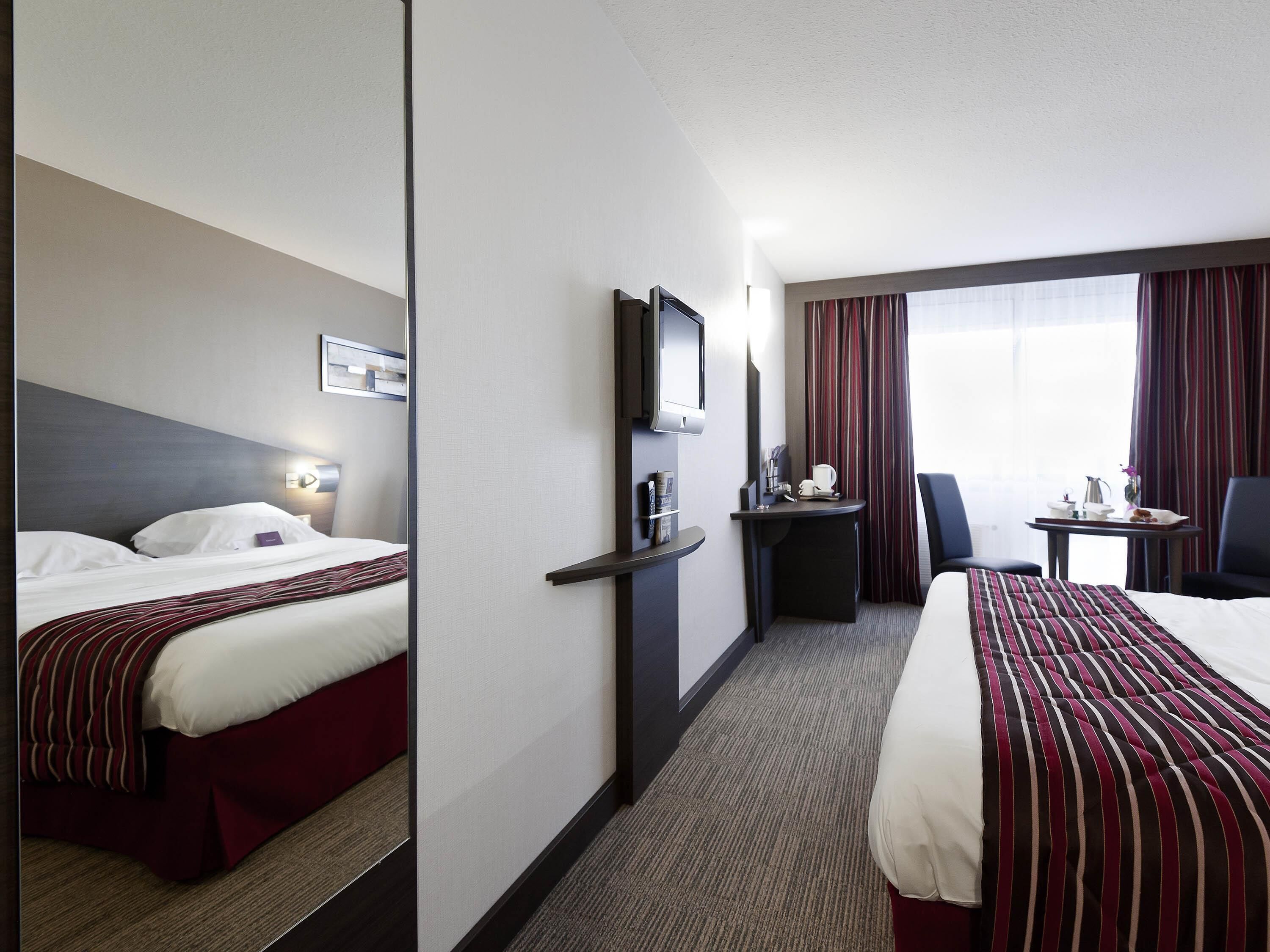 A hotel room with a bed, a desk, a chair, a TV, and a window with curtains.