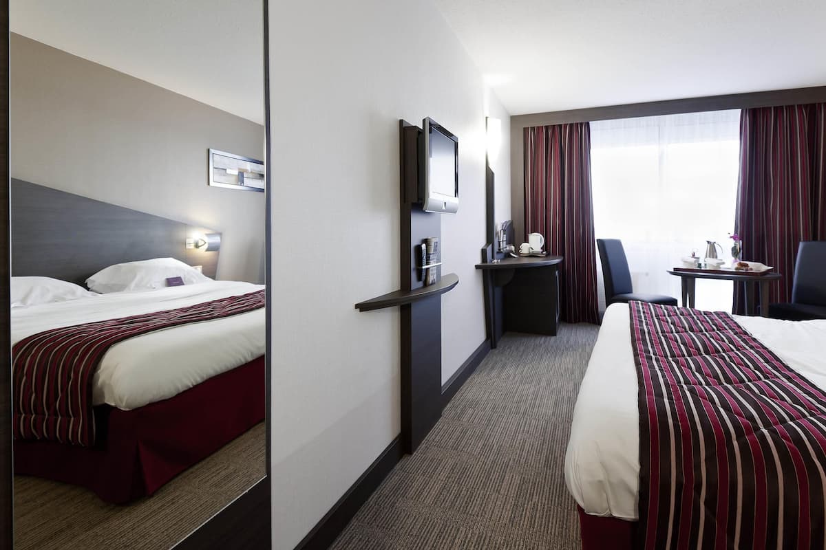 A hotel room with a bed, a desk, a chair, a TV, and a window with curtains.