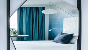 Un dormitorio moderno con una cama, una mesita de noche con una planta, un candelabro colgante y cortinas color turquesa.