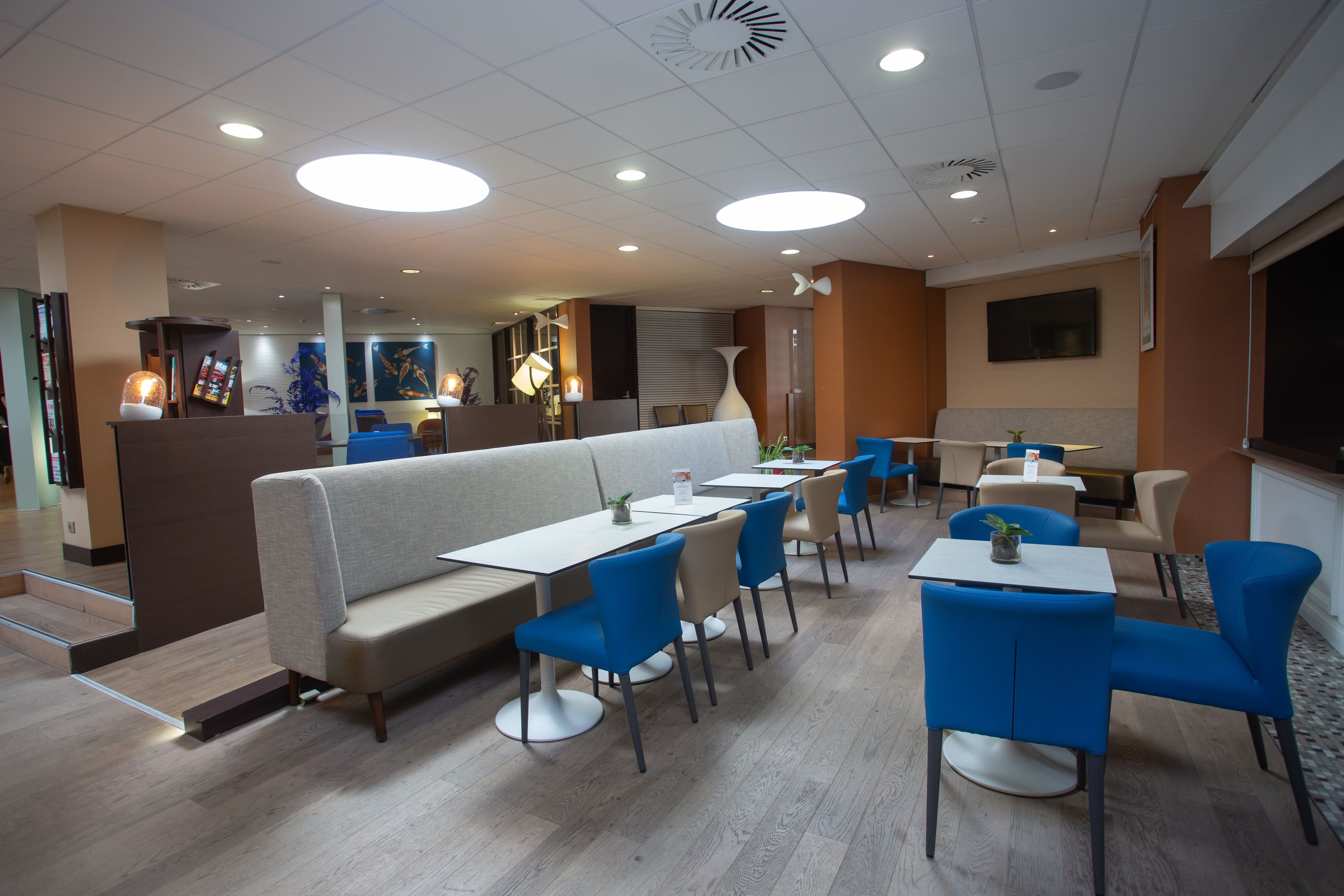 En modern restaurang med olika typer av sittplatser, inklusive avskilda bås och bord, en central bardisk och en platt-TV som är monterad på väggen.