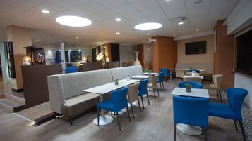 En modern restaurang med olika typer av sittplatser, inklusive avskilda bås och bord, en central bardisk och en platt-TV som är monterad på väggen.