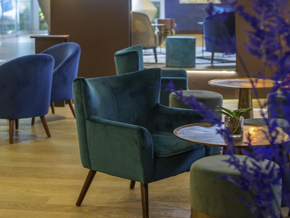 A modern interior with teal chairs and round tables, wooden flooring, and a view of the outdoors.