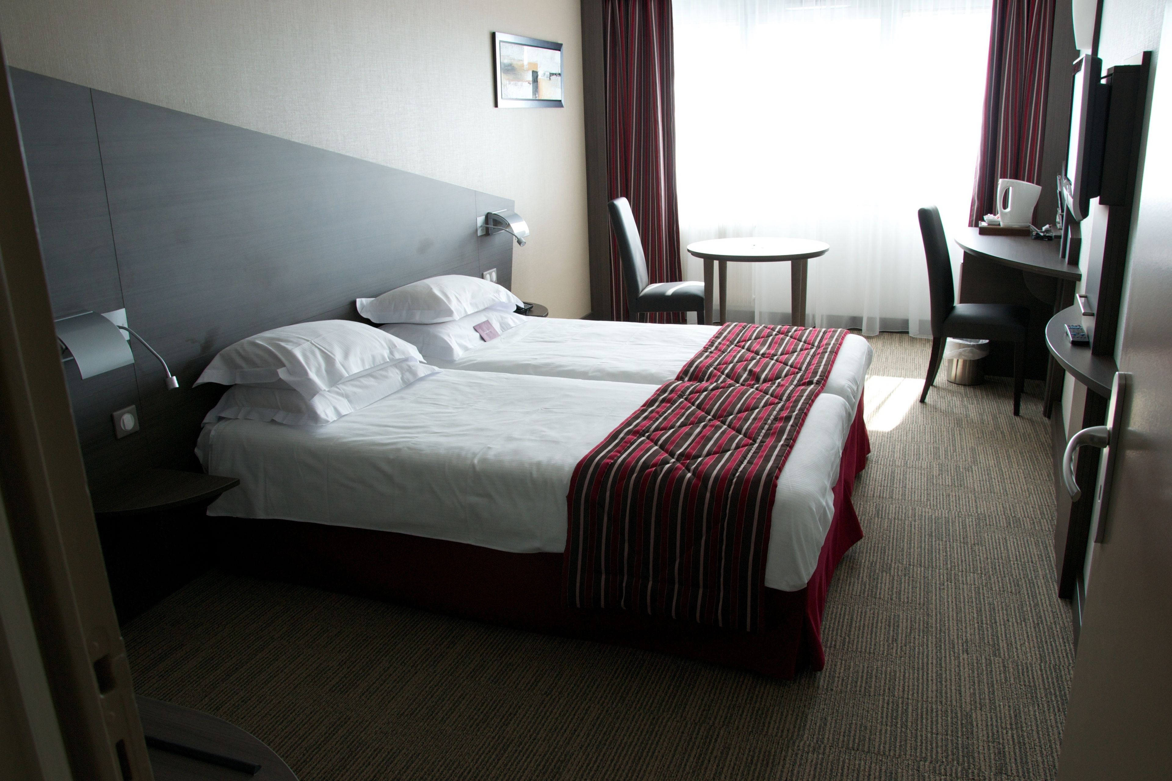 Une chambre d’hôtel avec deux lits, un bureau, une chaise, une petite table et un téléviseur.
