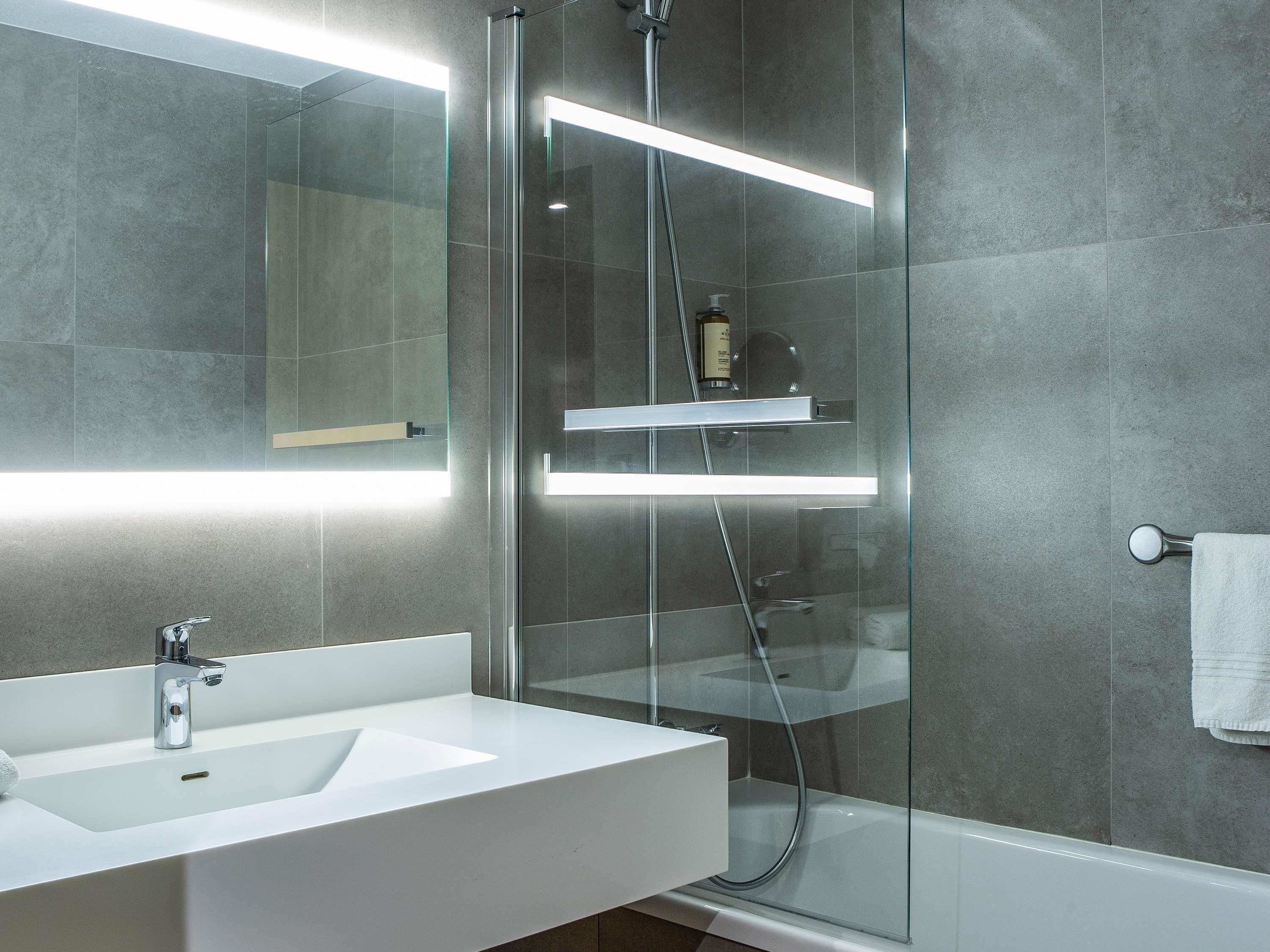 Une salle de bain moderne avec une douche à parois de verre, un lavabo blanc et un miroir.