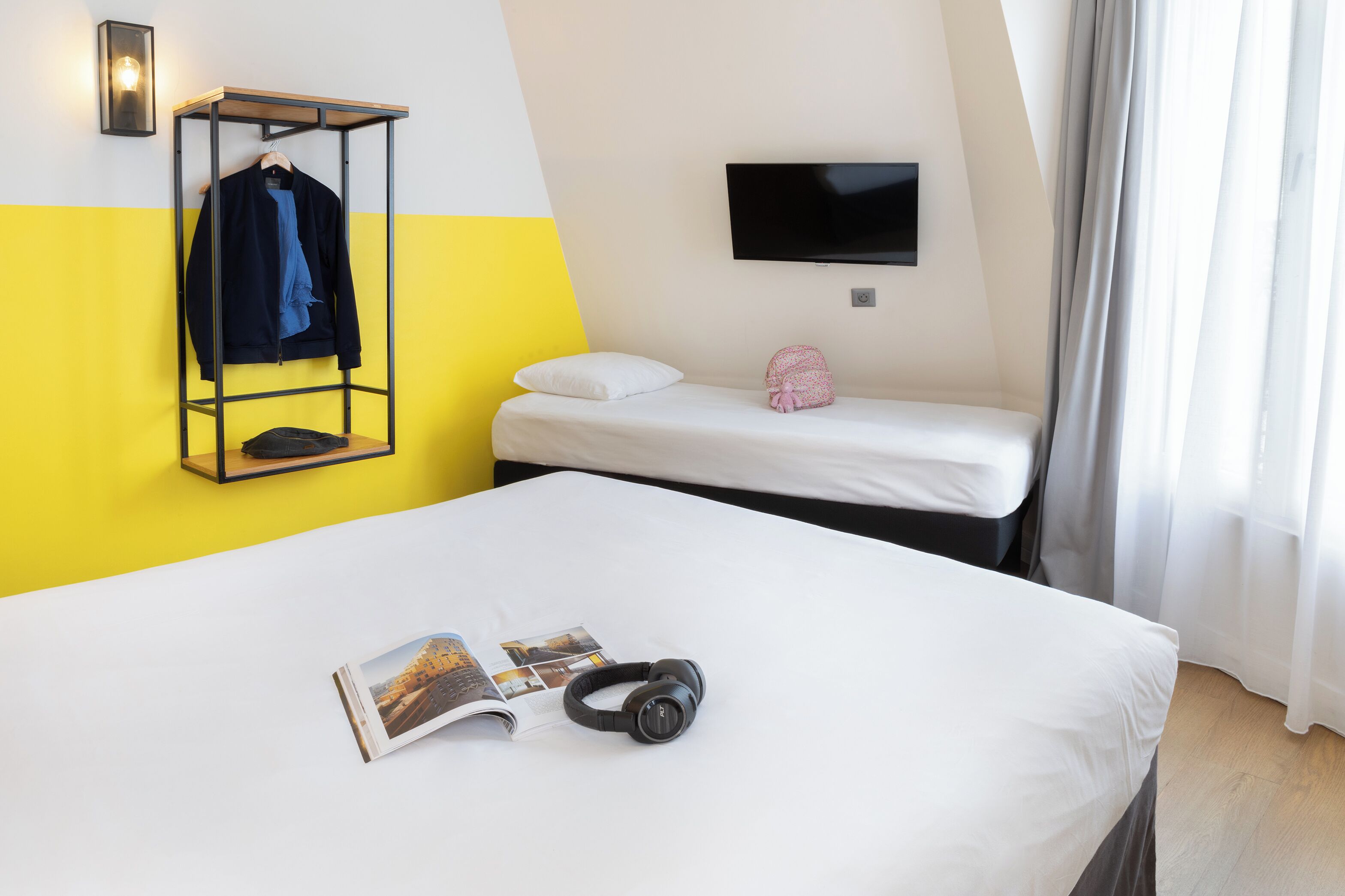 A hotel room with a bed, a hanging coat rack, a TV, and a window with curtains.