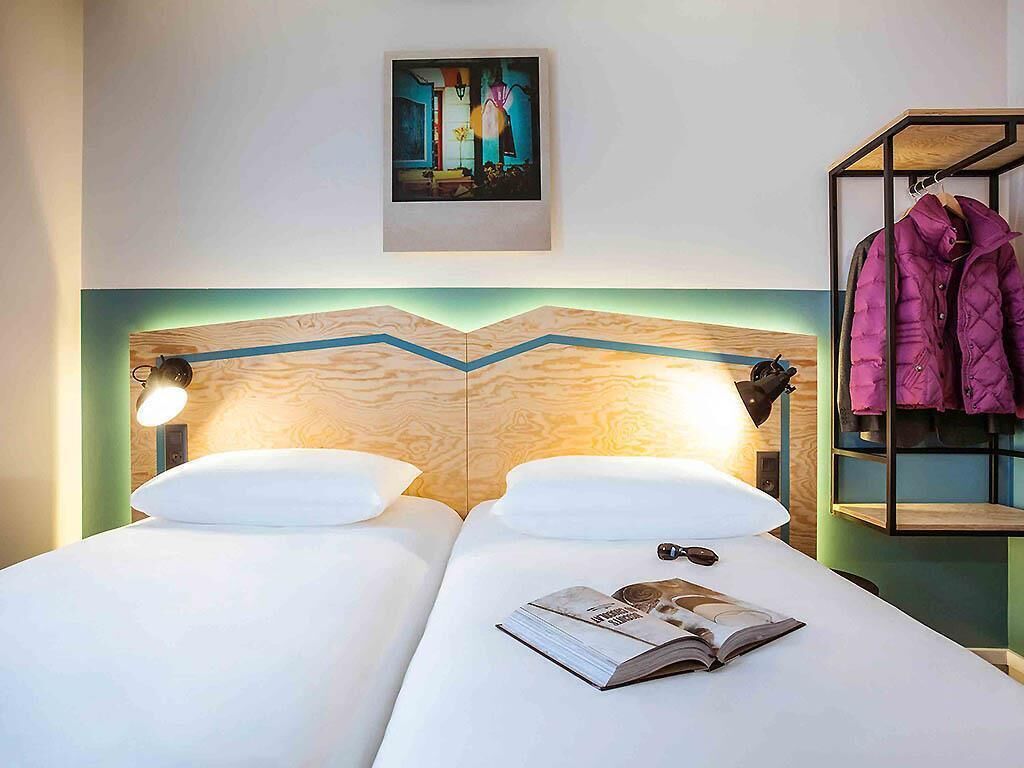 Habitació d'hotel amb dos llits, un panell de fusta al capçal, un quadre a la paret, una làmpada i un penjallabecs amb una jaqueta.
