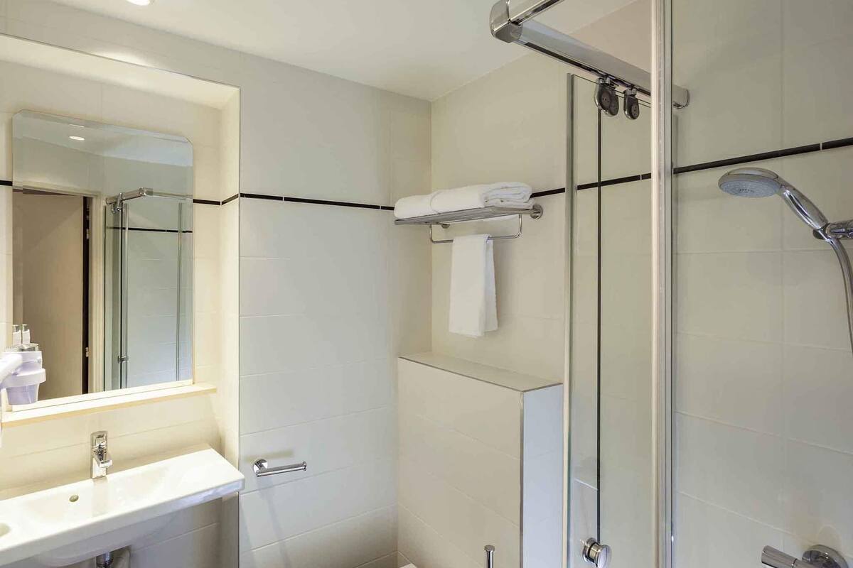 A modern bathroom with a glass shower enclosure, a sink with a mirror, and a towel rack.