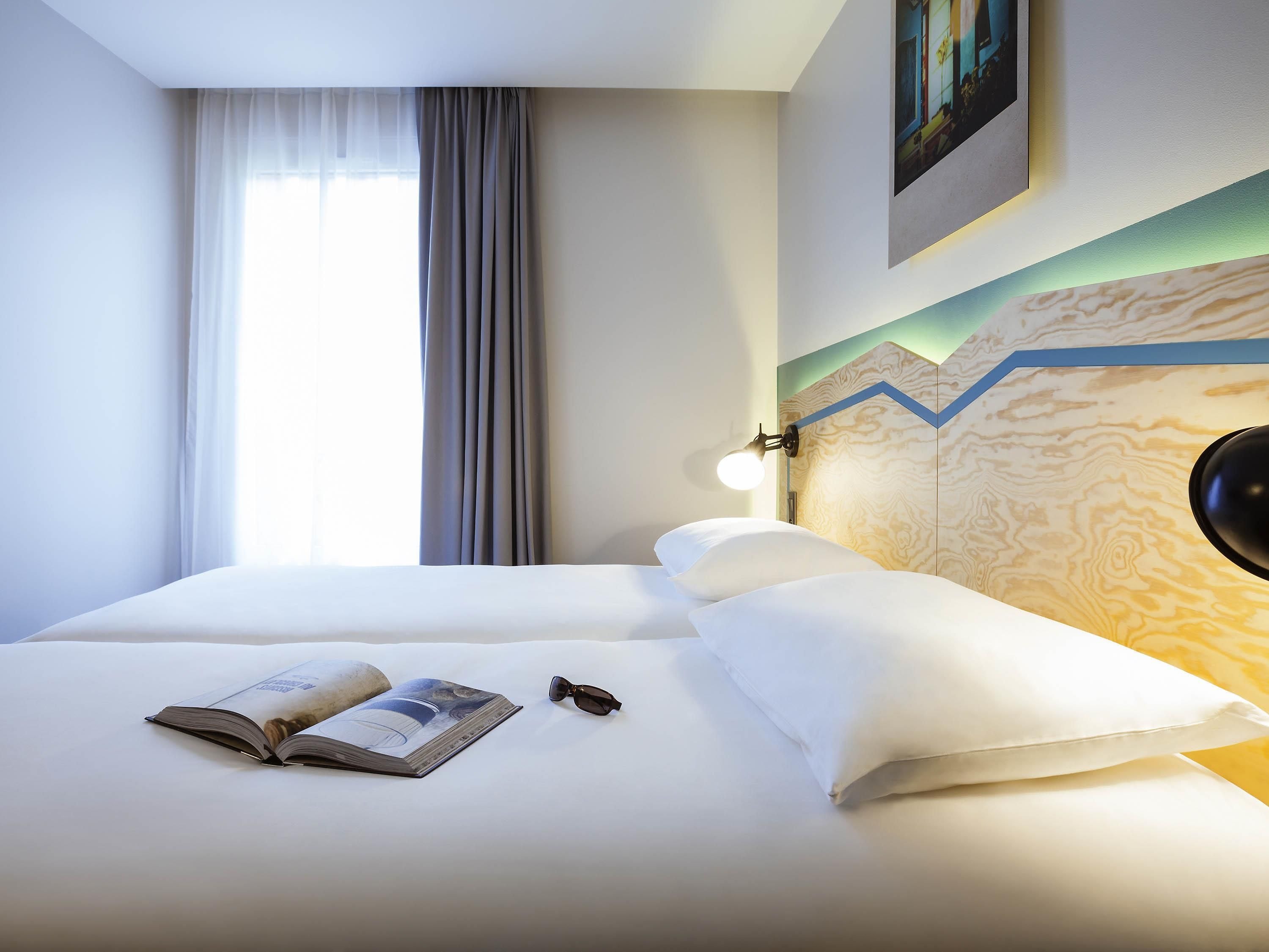 A hotel room with a bed, a book, and a pair of glasses on the bed.