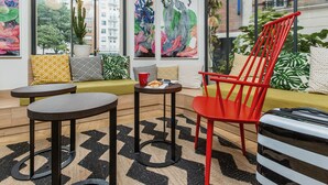 A modern living room with a red chair, a sofa, a small table, and a large window with city views. - ibis Styles Paris Nation Porte De Montreuil (Paris)