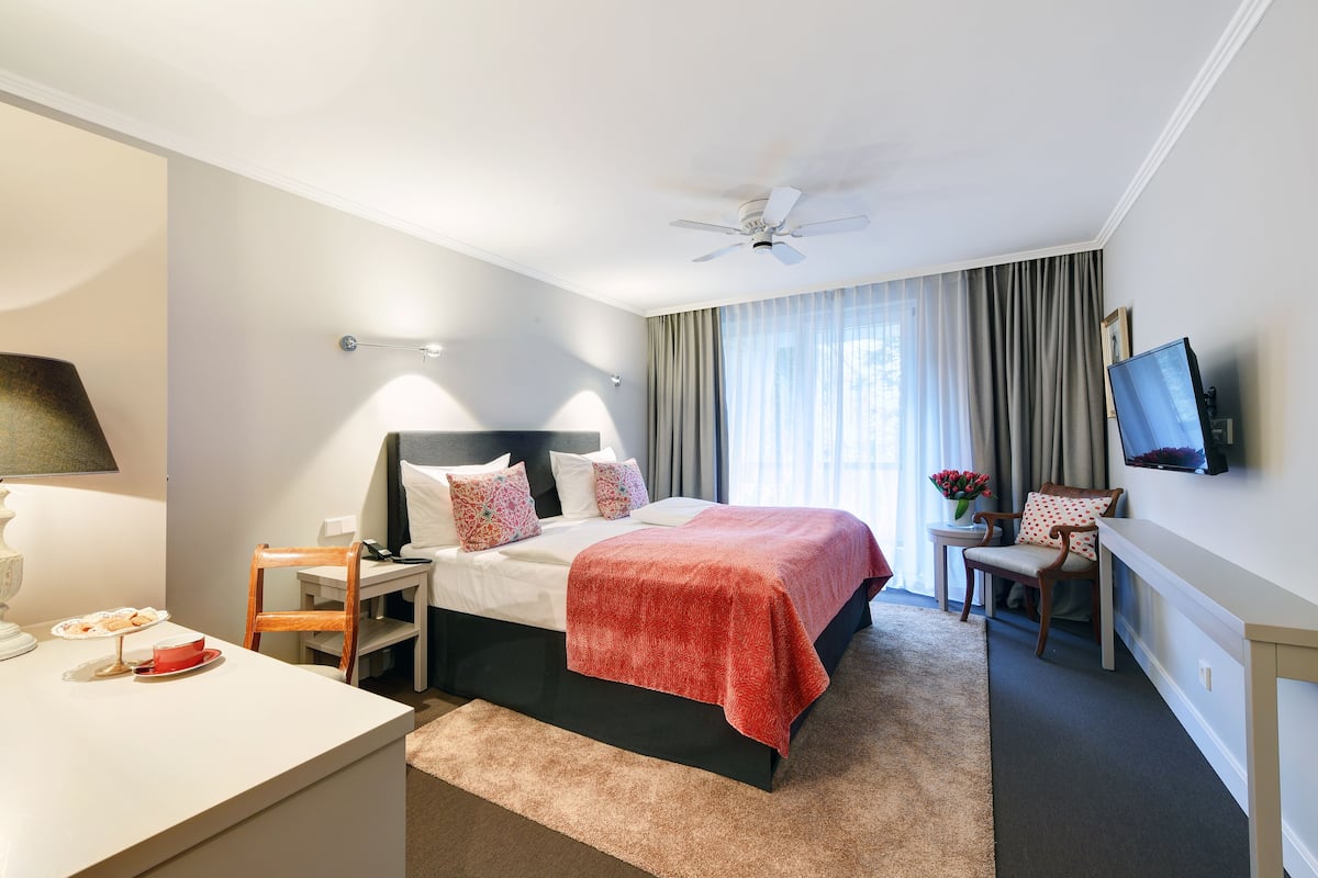 A hotel room with a bed, bedside table, chair, TV, and a desk with a lamp.